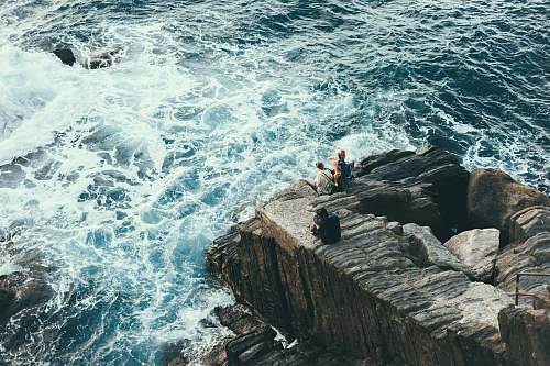 sea people sitting on rock formation on seashore coast