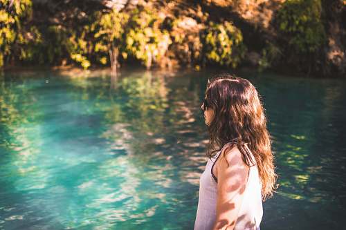 water woman wearing white tank top walking beside body of water during daytime girl