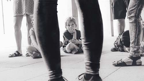 person grayscale photography of boy sitting on the floor watching the person in front of him people