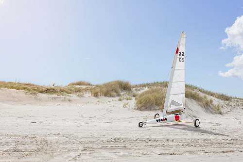 sea landscape photo of white sailboat with wheels on sand dunes