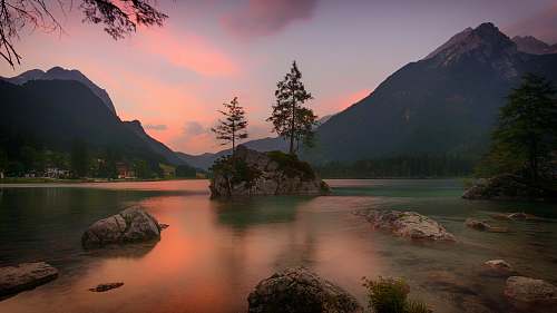 outdoors landscape photography of tree on rock formation surrounded by body of water near mountain during sunset tree