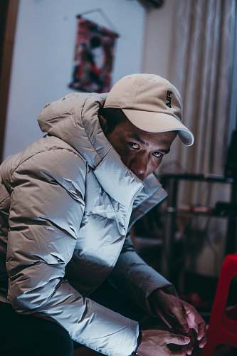 clothing selective focus photography of sitting man wearing bubble coat hat