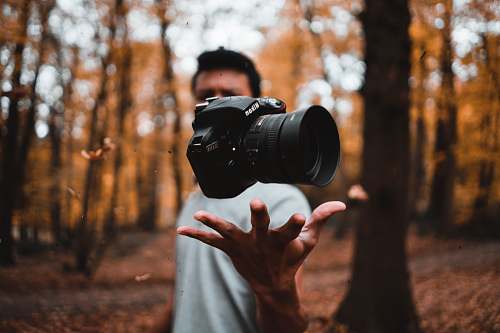 person black DSLR camera floating over man's hand at the woods electronics