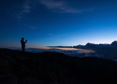 cloud silhouette of man taking photo on rock cliff mountain