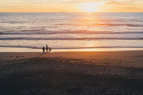 beach golden hour photography of three people on beach water
