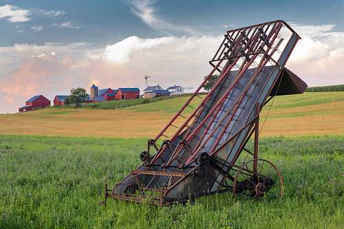 farm grey and red metal harvester machine on green field barn