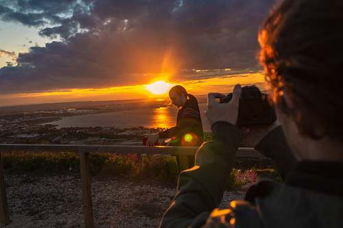 light man taking photo of man beside railing under gray and orange cloudy sky with sun nature