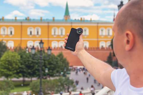 person man holding phone near building and trees cell phone
