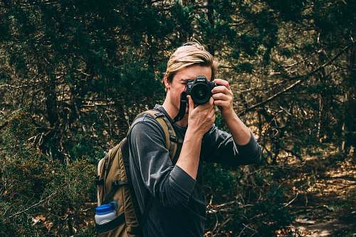 person man in sweater carrying brown backpack and holds black DSLR camera camera