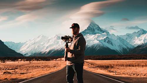 person man standing on asphalt road holding camera photo