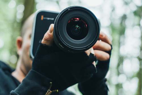 person person holding camera while standing near forest trees camera