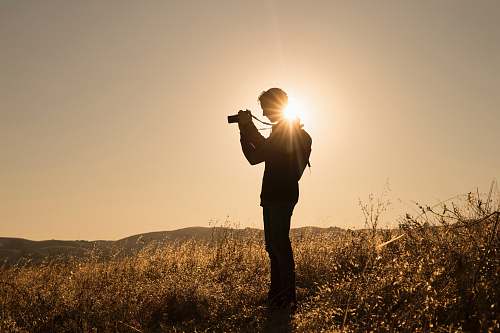 person silhouette of person holding camera on brown fields during daytime photography