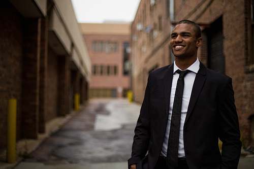 people smiling man standing between brown concrete buildings at daytime person