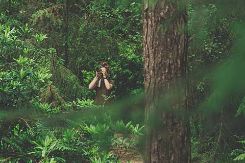 person woman in green dress taking picture in the woods tree