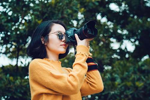 person woman taking photo near tree sunglasses