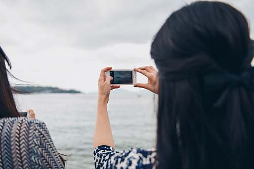 person woman using smartphone in front of seawater women