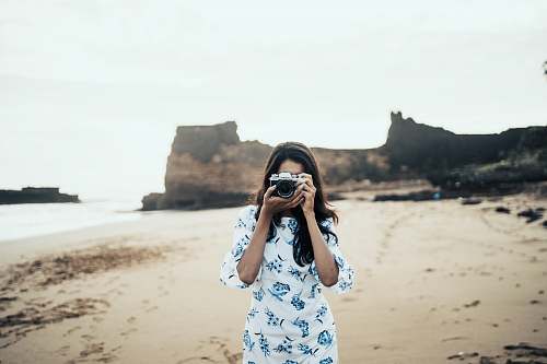 person woman wearing white and blue floral dress holding black and gray camera diu