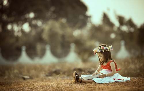 person girl sitting whil holding book on field reading