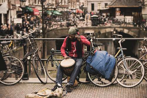 person man in red shirt playing darbuka drum while sitting on gray bike near at deck rail bicycle