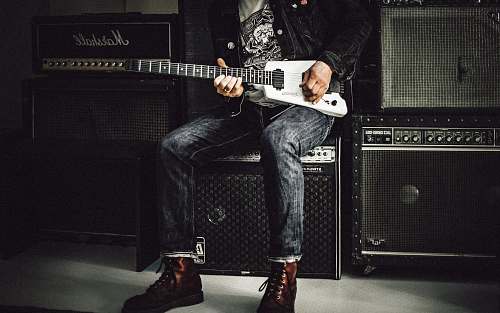 music man wearing blue denim jeans playing white and black electric guitar sitting on black guitar amplifier musician
