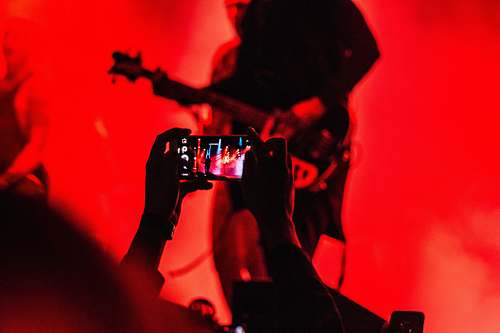 music person holding smartphone in front of a person playing guitar on stage phone