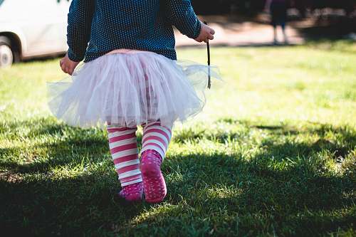 kid toddler girl wearing teal and white polka-dot long-sleeved shirt and white tutu skirt outfit walking on green sod at daytime tutu