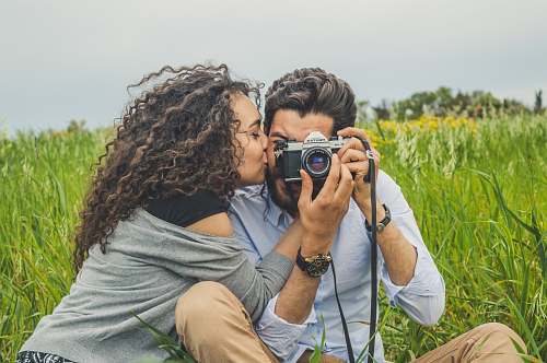 human man and woman sitting on grass field holding camera camera