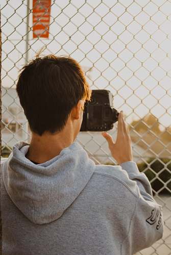 human man in grey hoodie taking photo near chain link camera