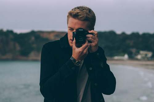 human shallow photography of man holding camera people