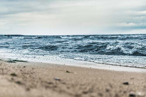 water low-angle photography of brown sand beside body of water under white and blue sky at daytime sea