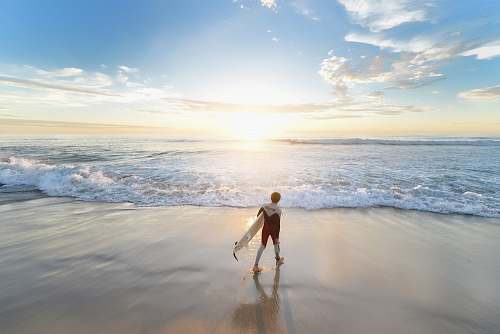 water man holding surfboard walking on shore during daytime ocean