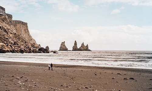 sea two person walking on seashore under clear blue sky water
