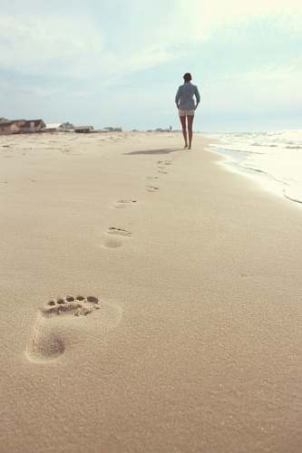 footprint woman wearing blue dress shirt and white short shorts walking on seashore woman