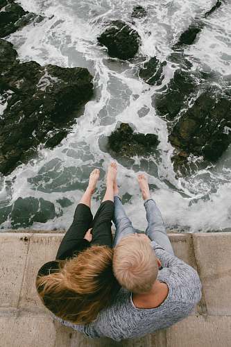 ocean man and woman sitting on cliff near body of water sea