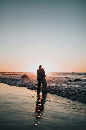 human silhouette photo of couple standing on beach watching sunset person