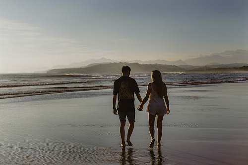 beach man and woman holding hands while walking on body of water coast