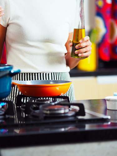hand person holding bottle of oil at gas stove frying pan