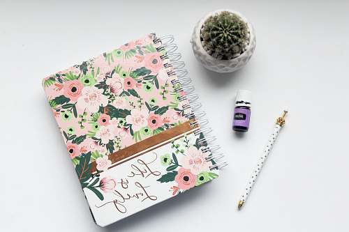 book white and pink floral notebook on table pen
