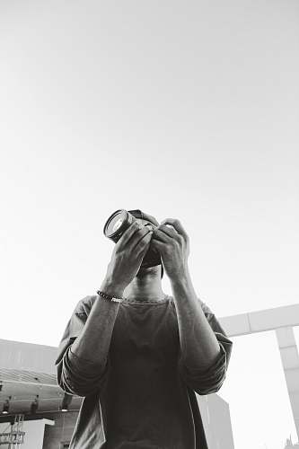 person grayscale photography of man standing and holding DSLR camera human