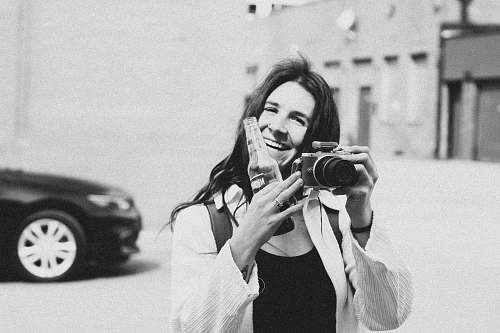 person grayscale photography of person smiling holding bottle and camera black-and-white
