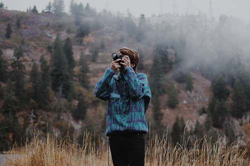 person man using black DSLR camera standing on grassfield photo