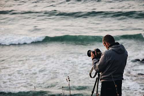 person person holding camera standing beside body of water photo
