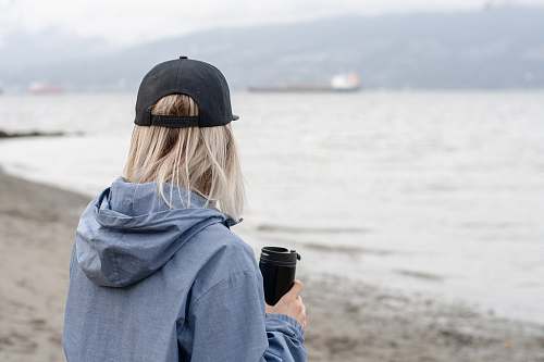 person woman standing beside beach while holding black tumbler photo