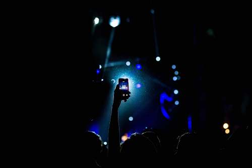 phone low light photography of person raising hand holding smartphone light