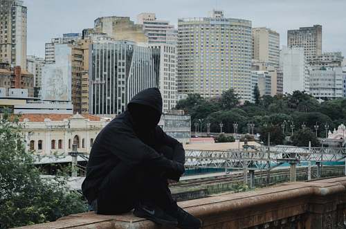 person man wearing hooded jacket sitting on beige concrete human