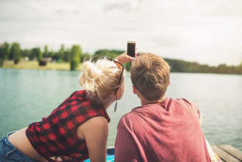 human woman and woman sitting on dock both holding one smartphone person