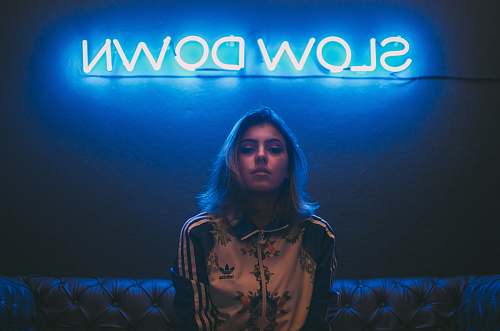 neon woman sitting on brown sofa under slow down neon signage sign