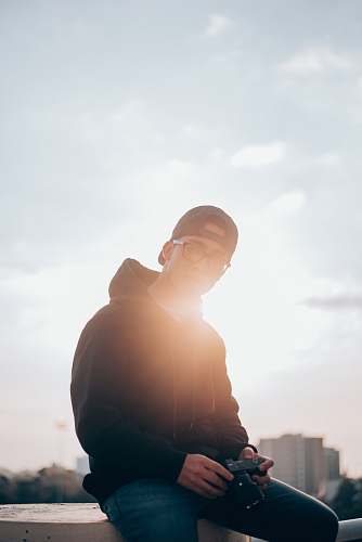human man in black hoodie sitting on railings holding camera flare