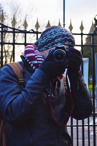 photographer man wearing black jacket using black Canon DSLR camera near black metal gate apparel