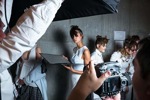 human person holding camera taking photo of woman standing near gray wall fashion